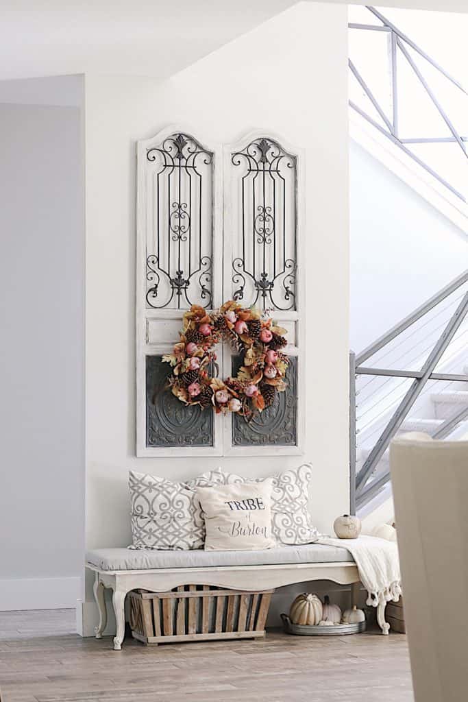 Front foyer with a Fall wreath hanging on gates on a wall. With a bench below it.