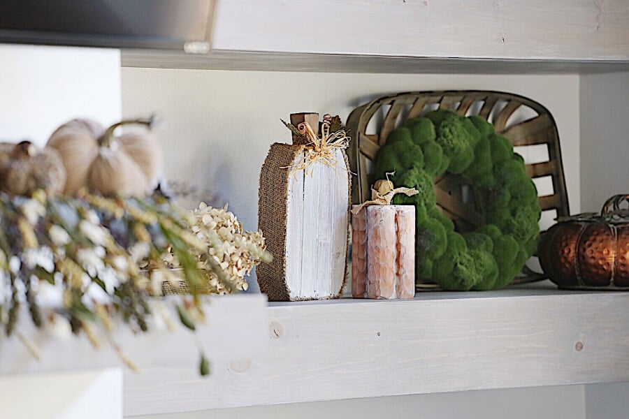 An open shelf on the wall with pumpkins that are wood and metal.