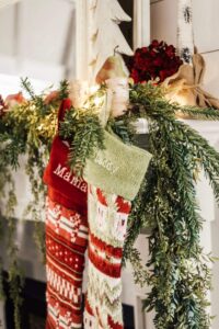 Festive holiday stockings hanging on a Christmas mantel decorated with greenery and string lights.