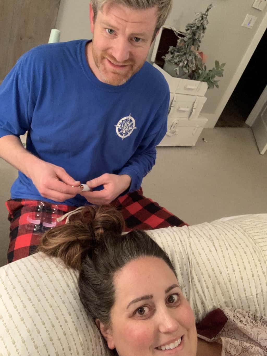 Man sitting on a chair at end of the bed when the woman laying on a pillow with her head toward him. He is getting the lash kit ready. They are in the bedroom.