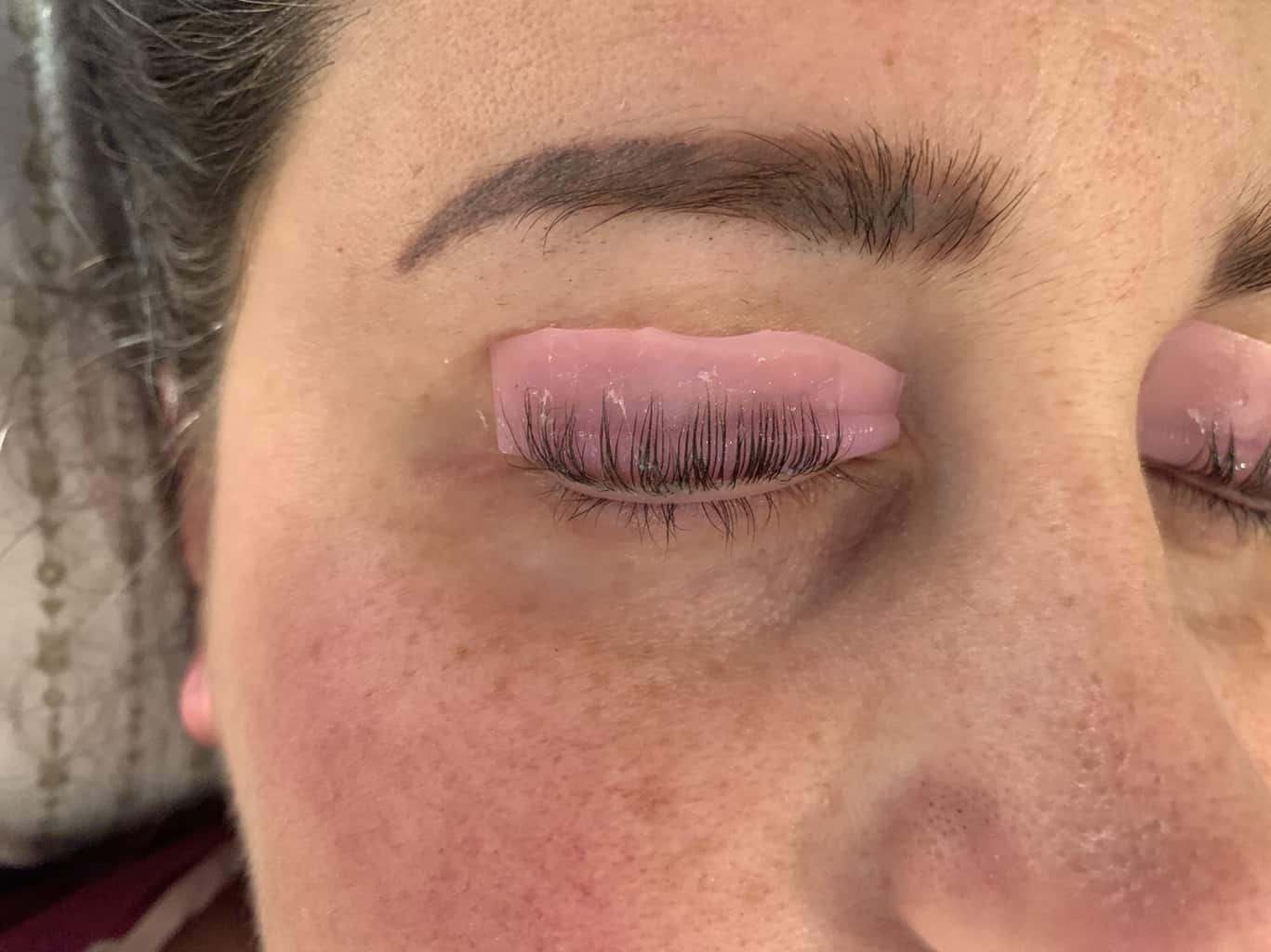 Close up shot of woman's face with her top diy lashes curled on a pink plastic thing from amazon eyelash lift diy.