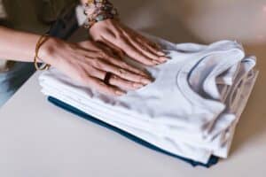 Stacked neatly white and navy t-shirts folded on a white surface. Woman's hands with jewelry smoothing the clothing.
