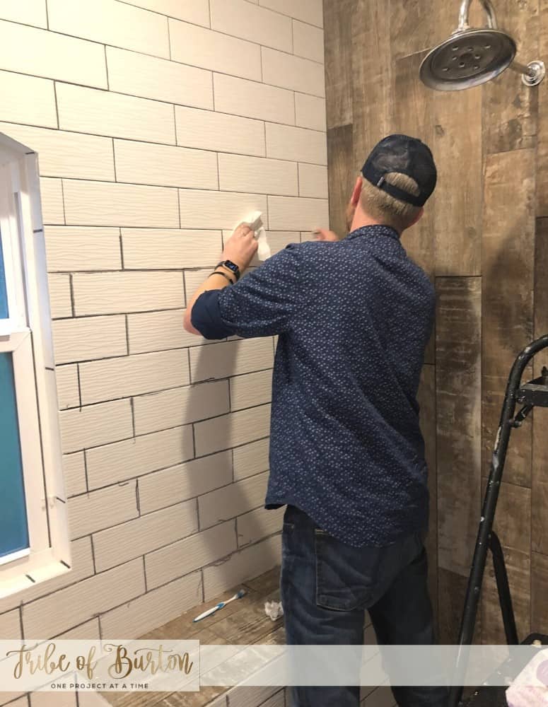 Man coloring bathroom shower grout lines grey.