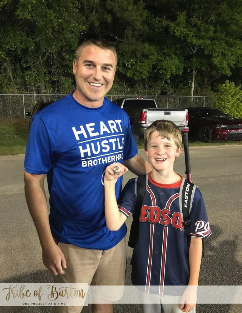 Boy holding up his championship ring with his batting instructor.