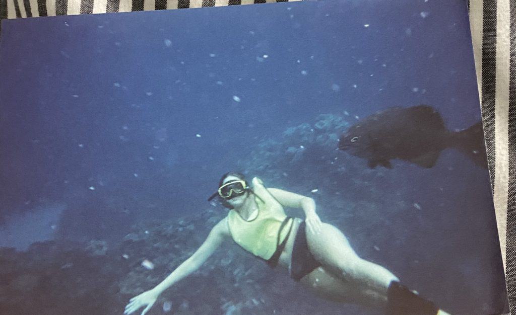 Photo of  girl snorkeling underwater with a fish behind her.