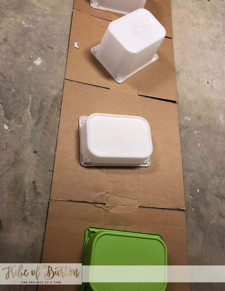 Plastic toy bins upside down laying on cardboard in a garage floor.