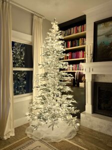 White snow-frosted Christmas tree decorated with lights in a cozy living room.